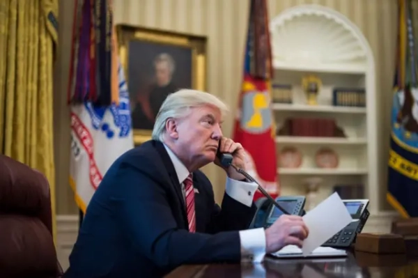 Трамп зі слухавкою телефону біля вуха, за столом Овального офісу