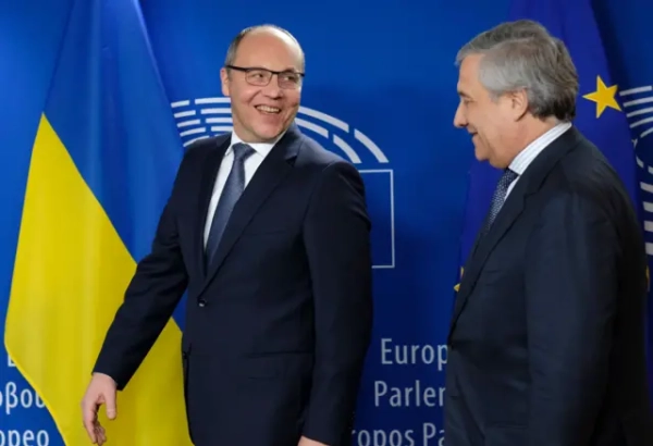 Усміхнений Парубій на тлі українського прапора та блакитного стенду з логотипом Європарламенту. Поруч стоїть у профіль Таяні