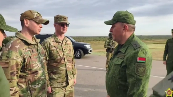 Двоє офіцерів в американській формі, один з них має шеврон із прапором США на плечі, інший — сонцезахисні окуляри. Навпроти — білоруський солдат із білоруським прапором на плечі.