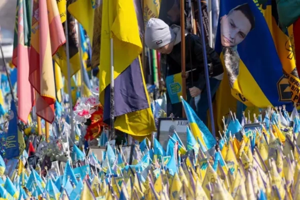 Хлопчик 5-6 років у кепці дивиться на жовто-блакитні прапори, встановлені на згадку про загиблих