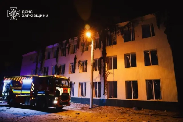 Біла триповерхова будівля з розбитими вікнами. Поруч стоїть пожежна машина.