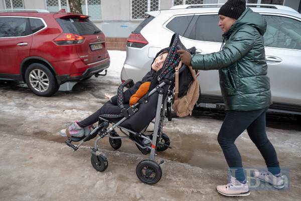 Мати Галина з донькою з інвалідністю Полею штовхає візок, вони прямують в Центр комплексної реабілітації, лютий 2026